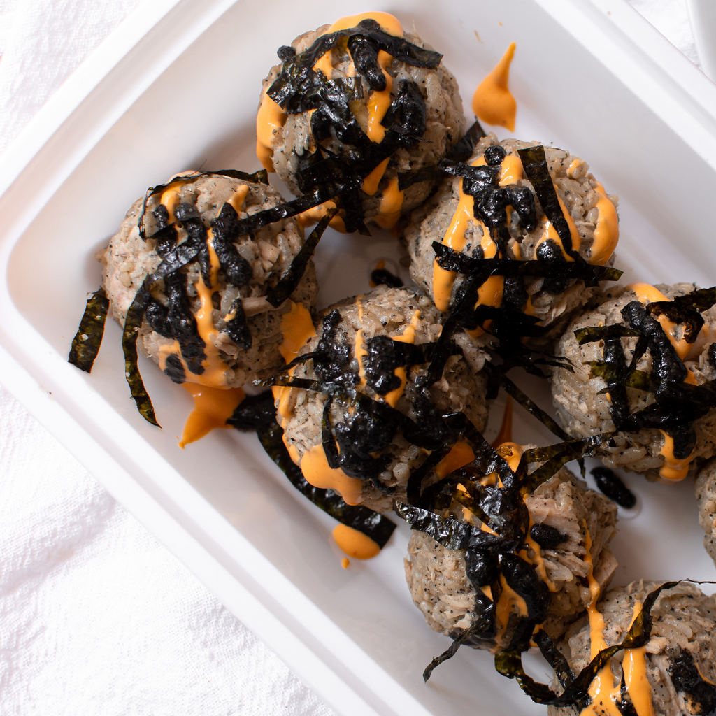 Eight sushi balls with beautiful black specs topped with strips of seaweed and orange spicy mayo. 