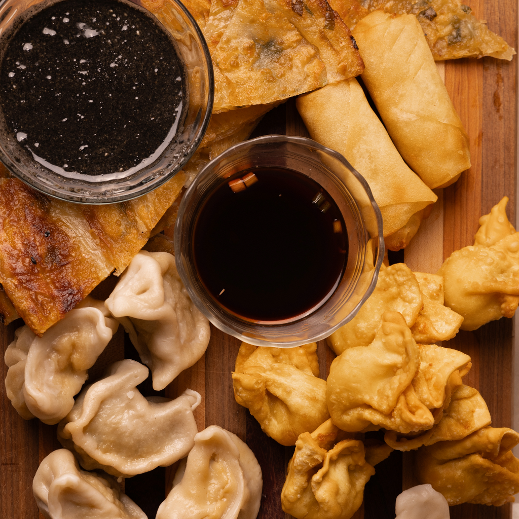 A charcuterie of fried egg rolls, dumplings, scallion pancakes and two small dishes of sauce. 