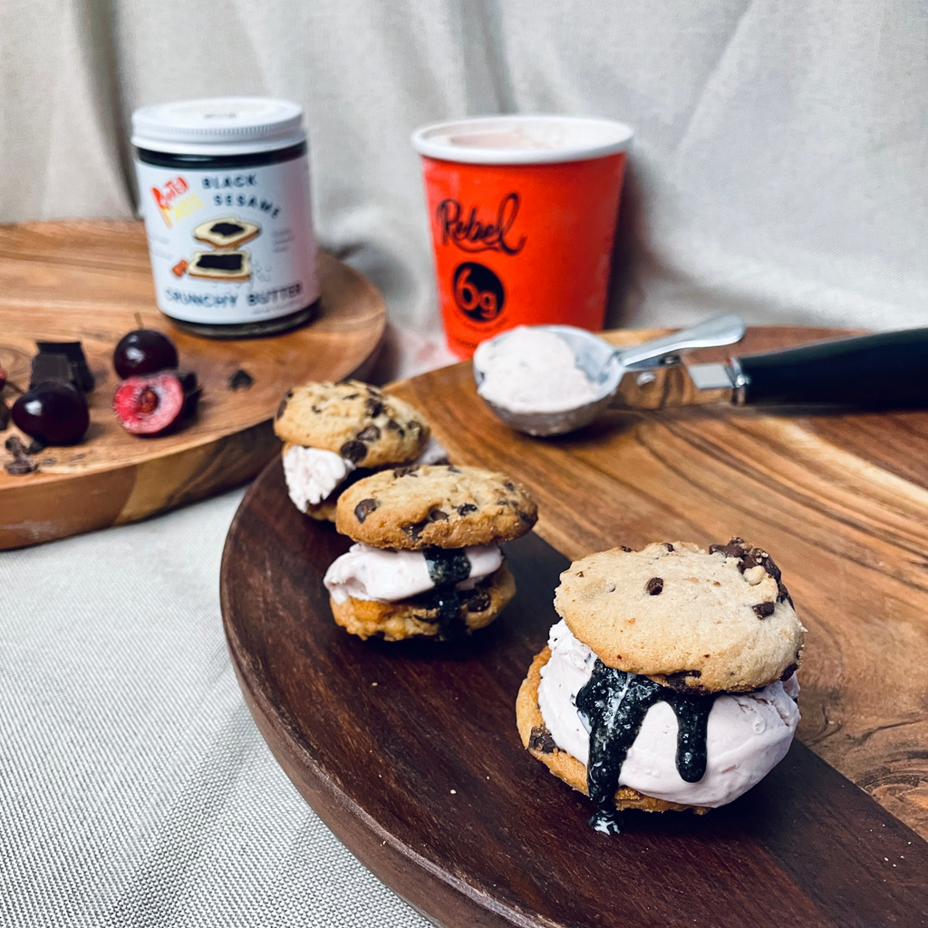 Three small, bit-sized ice cream sandwiches made with chocolate chip cookies, cherry chip ice cream, and Black Sesame Crunchy Butter are on wooden plates.