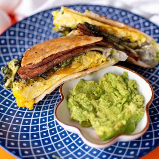 Cross-section of breakfast wrap to see the pan-fried spam, avocado, egg, and black sesame crunchy butter inside. Right next to it is a small bowl of freshly mashed avocado.